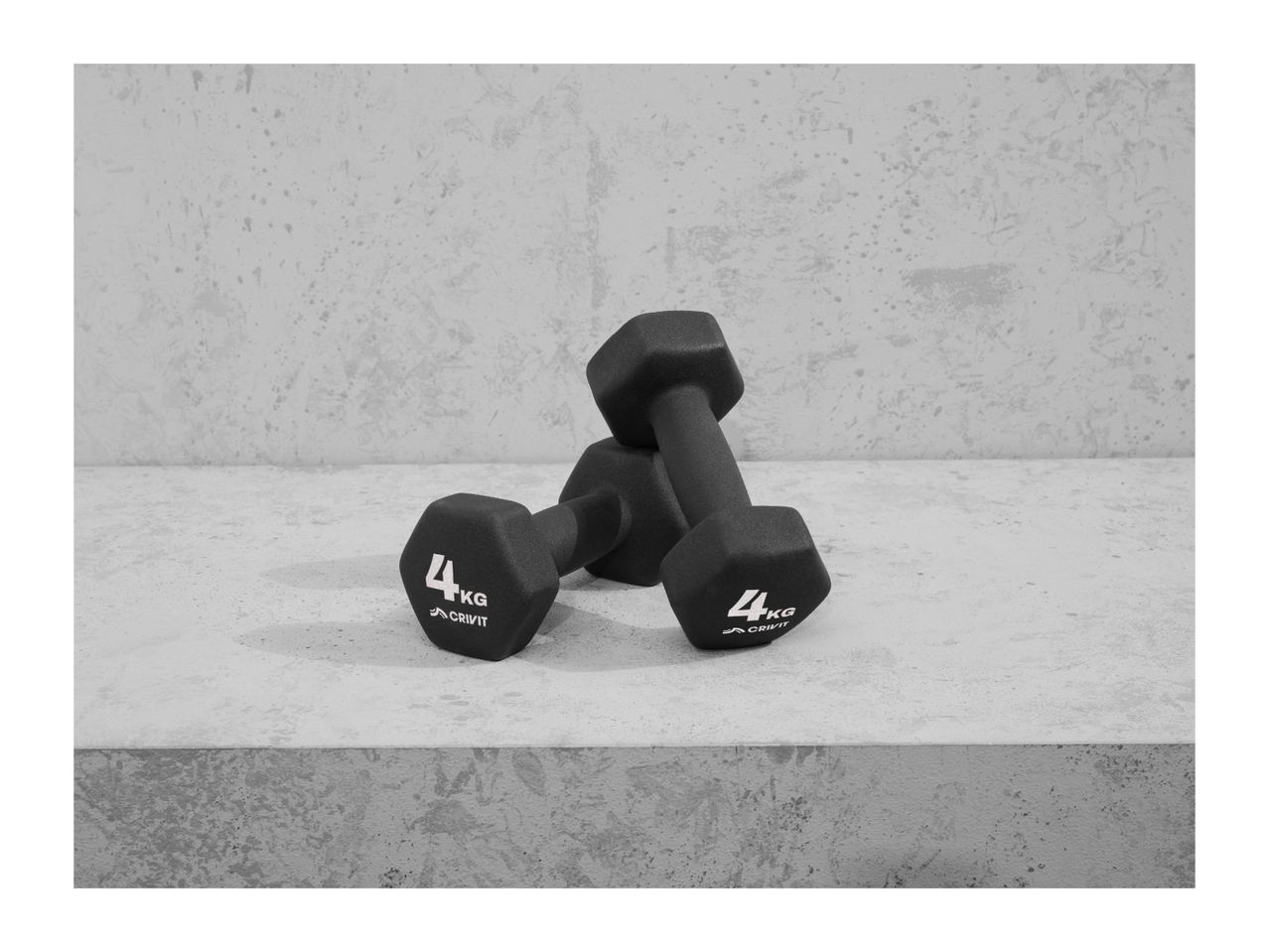 Two black 4kg Crivit dumbbells on a concrete surface.