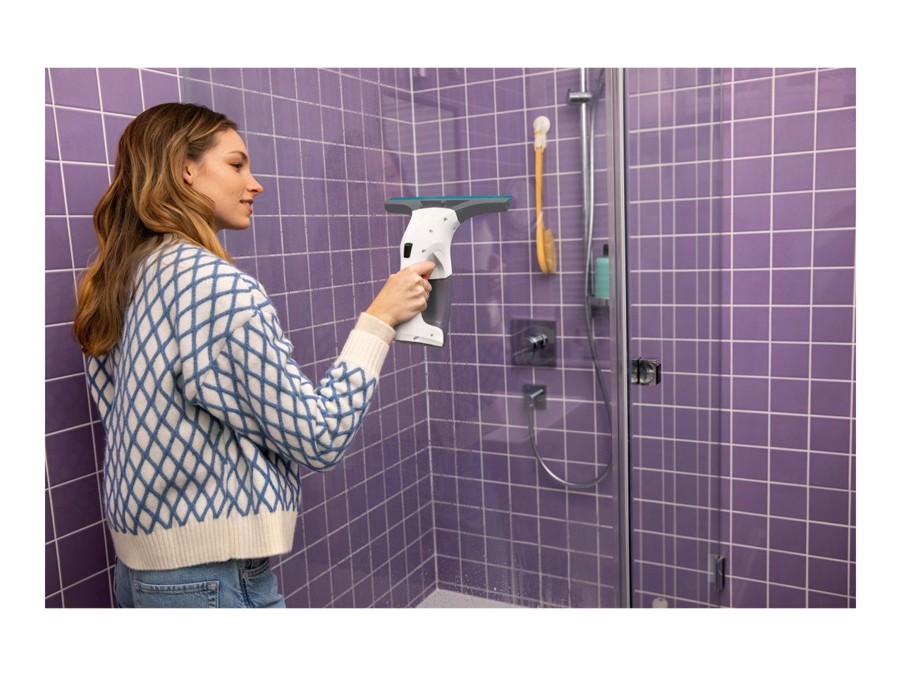 Woman cleaning a purple tiled shower with a window vacuum cleaner.