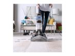 A person cleaning a dirty carpet with a Vax carpet cleaner in a living room.