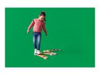 A young girl balancing on a wooden balance beam set with colorful pegs on a green background.