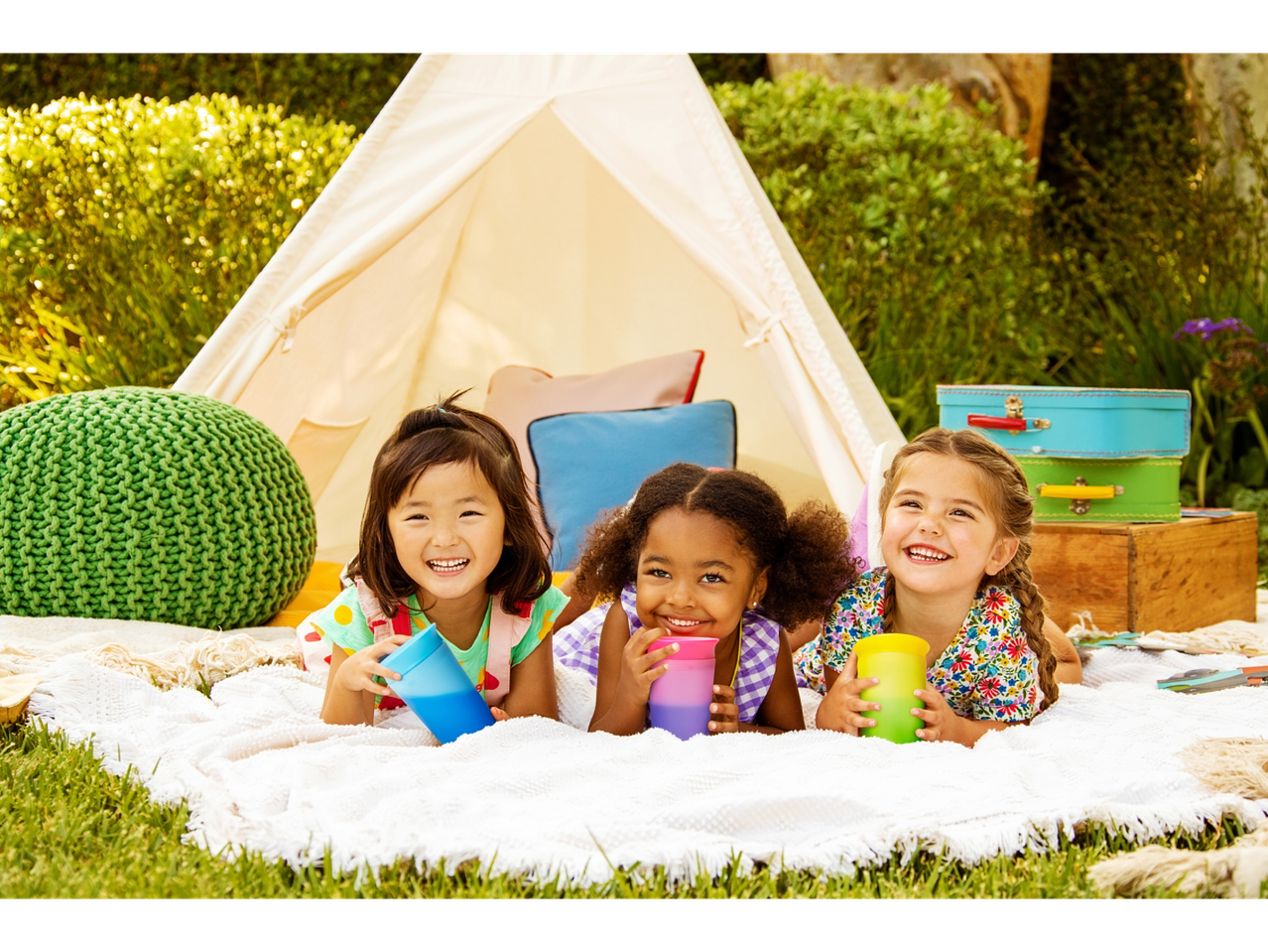 Three smiling girls with Munchkin Miracle 360° cups at a backyard picnic.