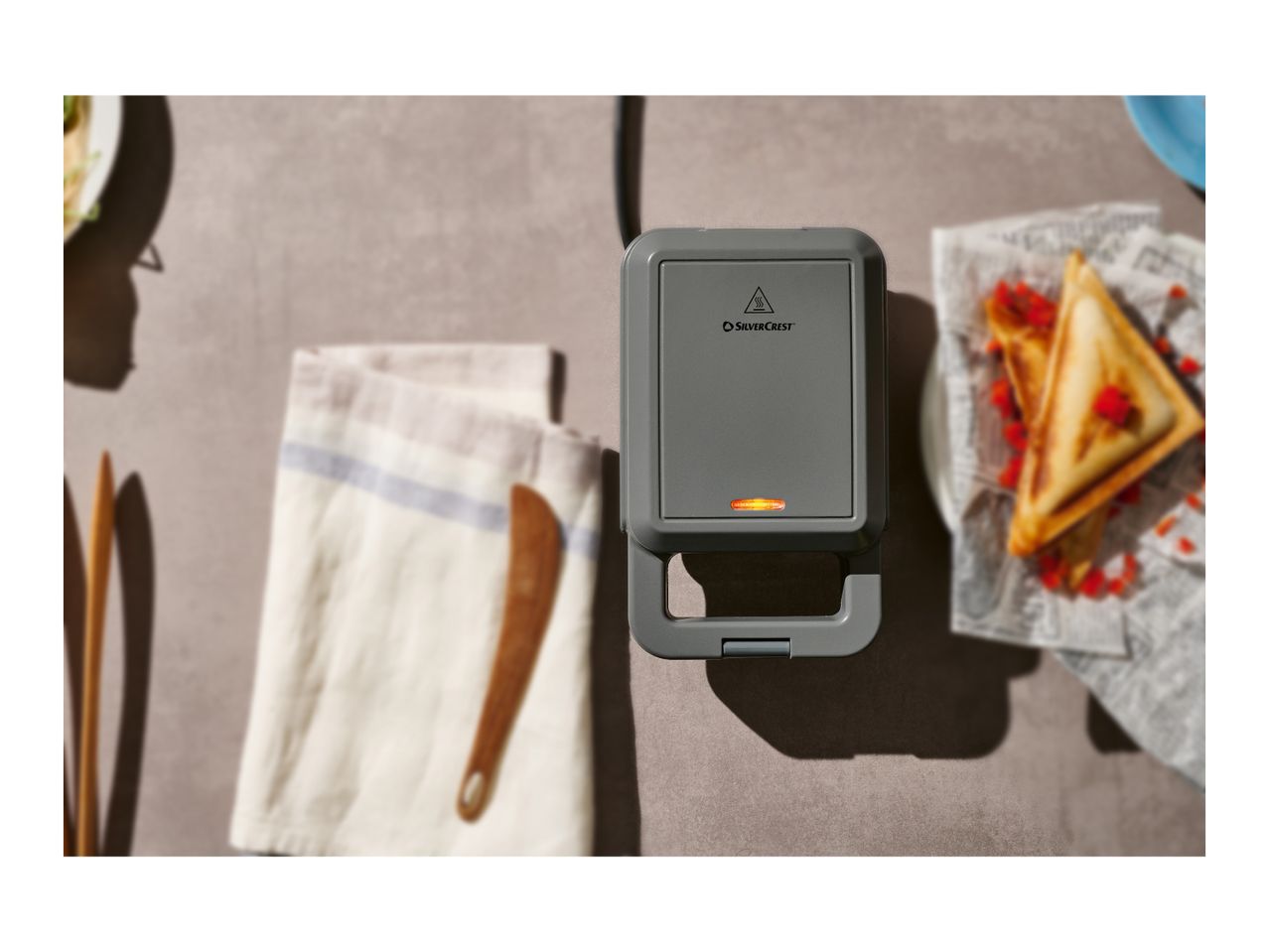 SilverCrest sandwich maker with cooked sandwiches and a towel on a table.
