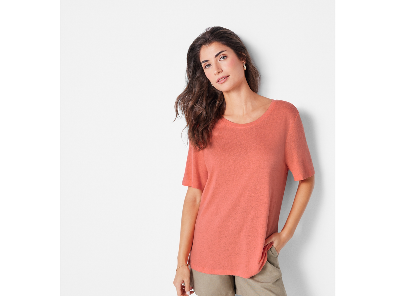 Ženski model v koralnem majici in bež kratkih hlačah.