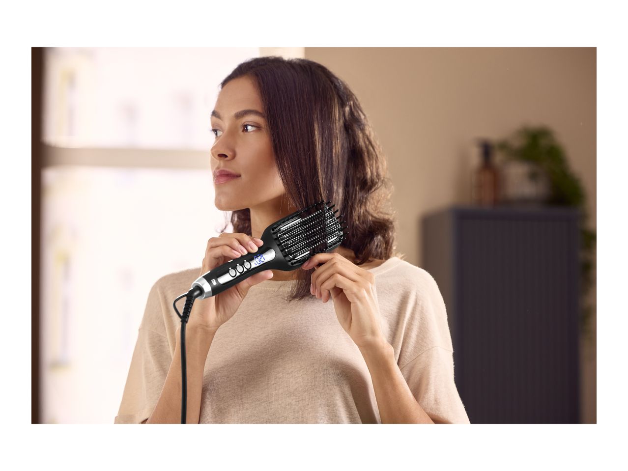 Woman styling her hair with a black heated hairbrush, looking to the side.