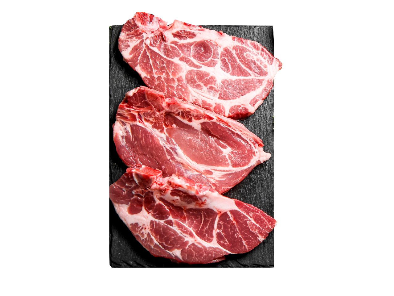 Trys šviežios kiaulienos kotletų ant juodos skalūno.