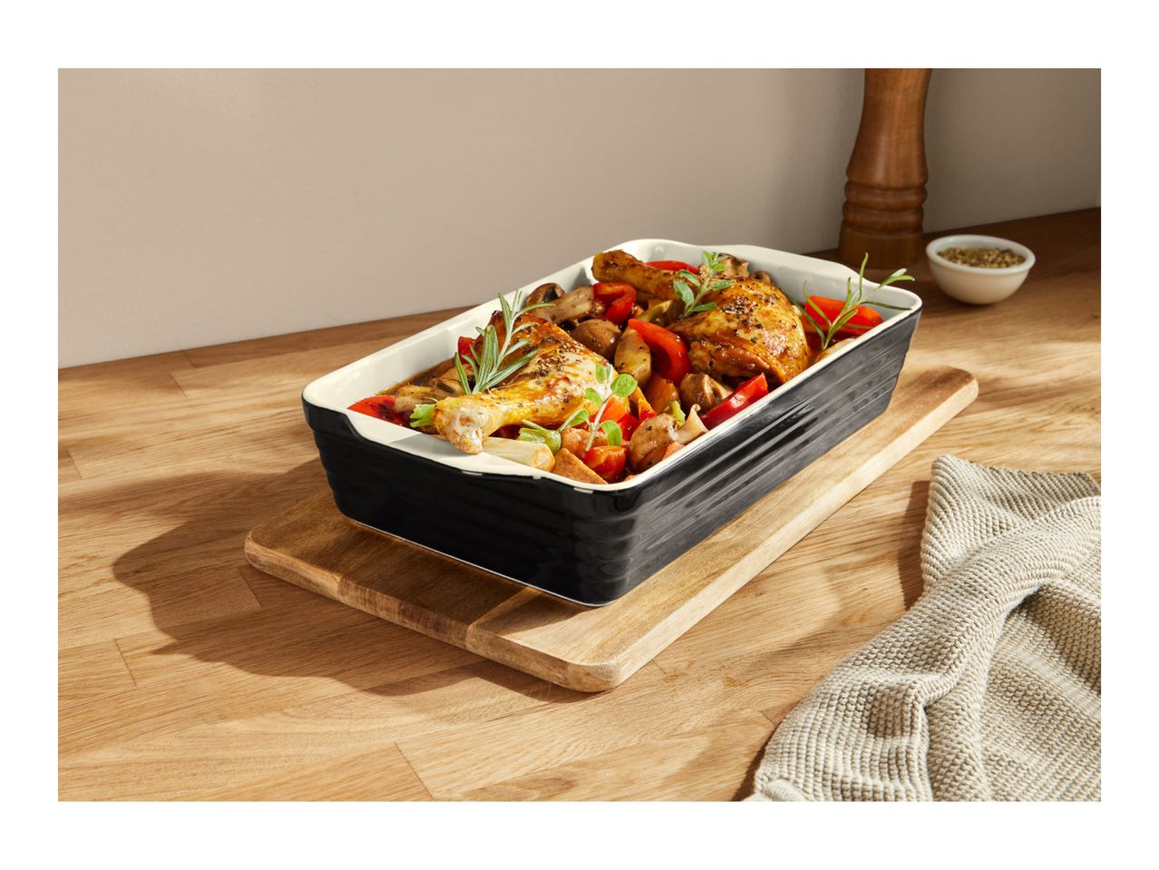 Roasted chicken and vegetables in a black baking dish on a wooden board.