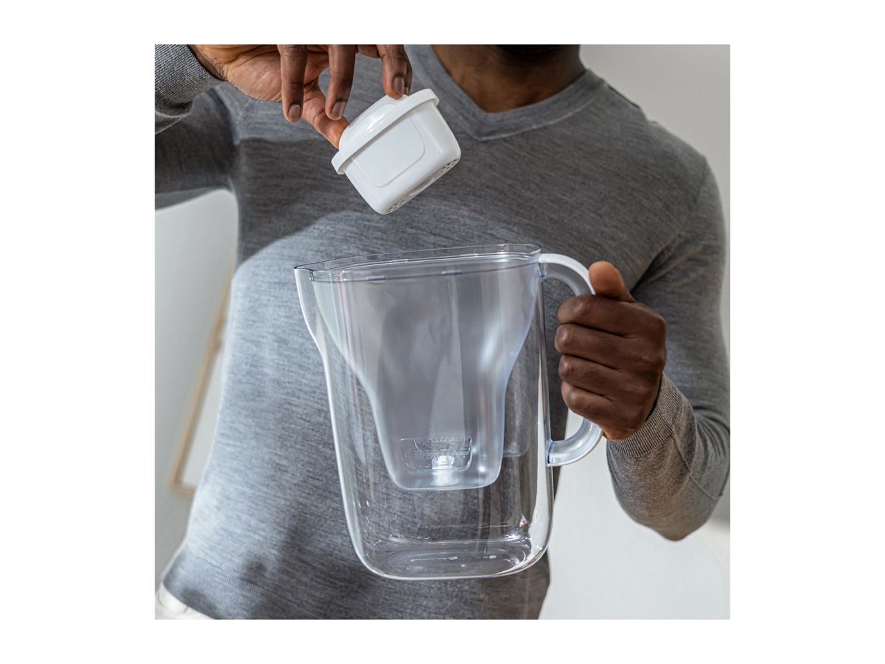 Person inserting a white water filter into a clear water filter pitcher.