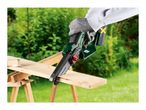 A person wearing protective gloves cuts a wooden plank with a cordless mini chainsaw.
