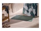 Green bath mat on tiled floor with shower curtain and wooden shelf with towels.