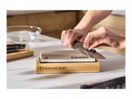 Hands sharpening a knife on a whetstone with a wooden base, next to a bowl of water.
