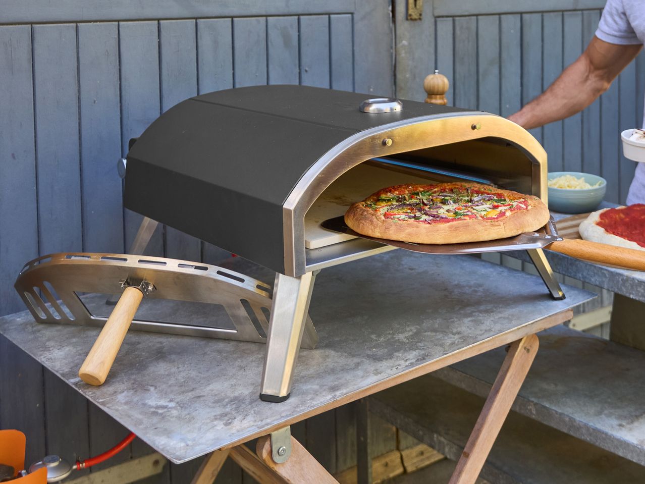 Outdoor pizza oven with a pizza being cooked, next to pizza ingredients.