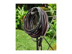 Garden hose coiled on a holder, with a connector, set against a green garden background.