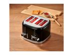 Black four-slice toaster with glowing heating elements on a wooden table next to toast and jam.