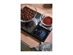 Digital kitchen scale with coffee beans and ground coffee in bowls, displaying measurements.