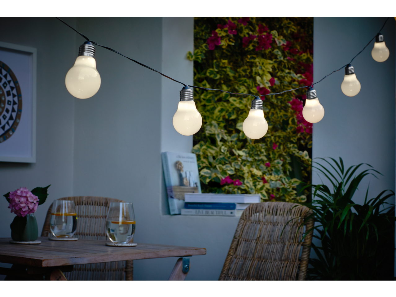 Outdoor string lights illuminating a cozy patio with a wooden table, chairs, and plants.