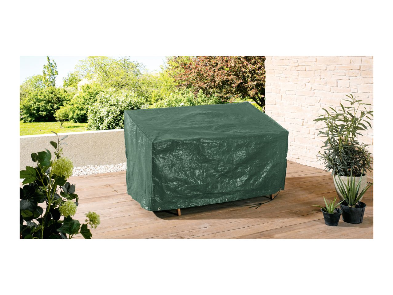 A dark green patio furniture cover sits on a wooden deck, surrounded by potted plants.