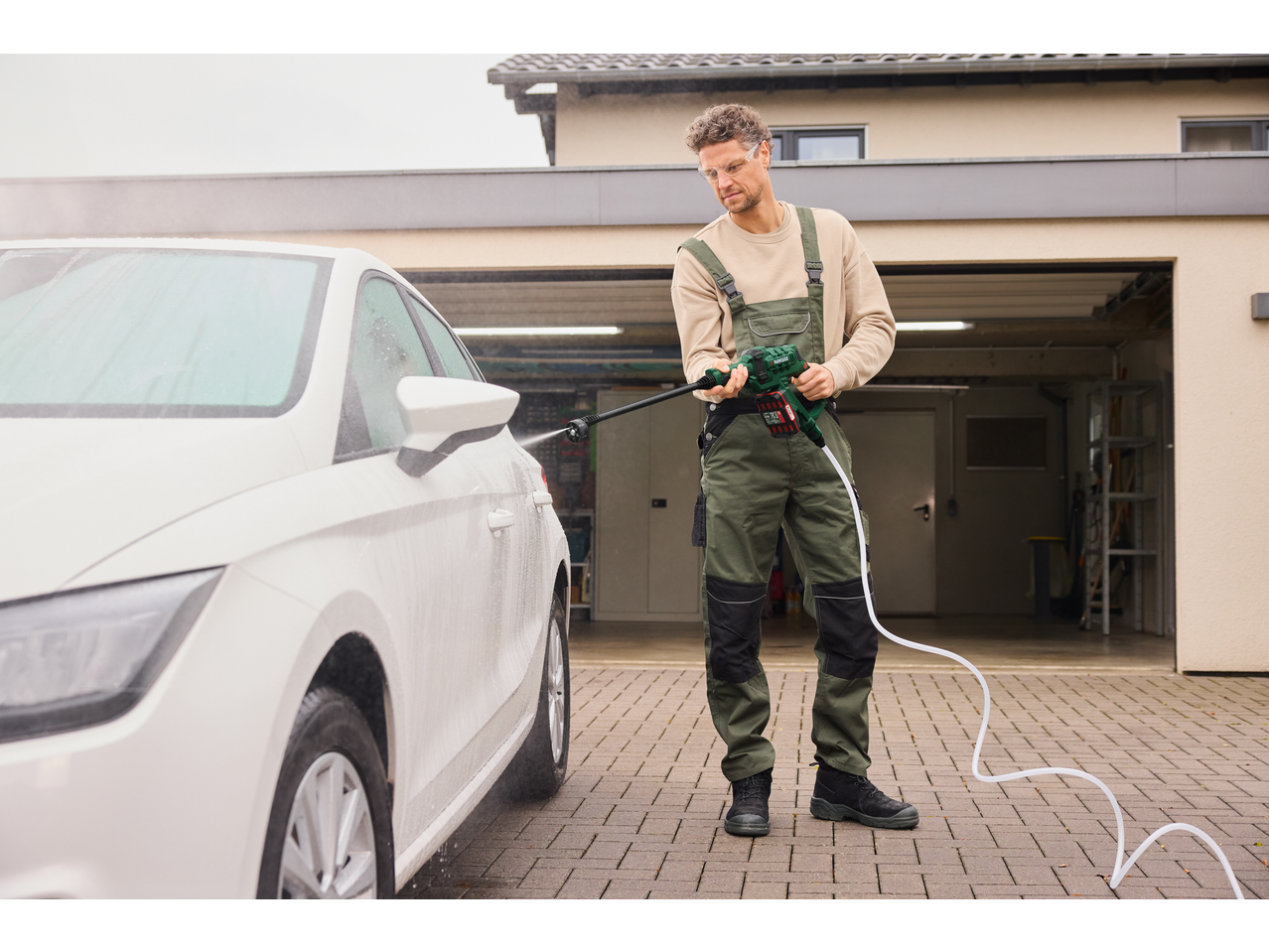 Homem a lavar um carro branco com um limpador de alta pressão a bateria PARKSIDE.