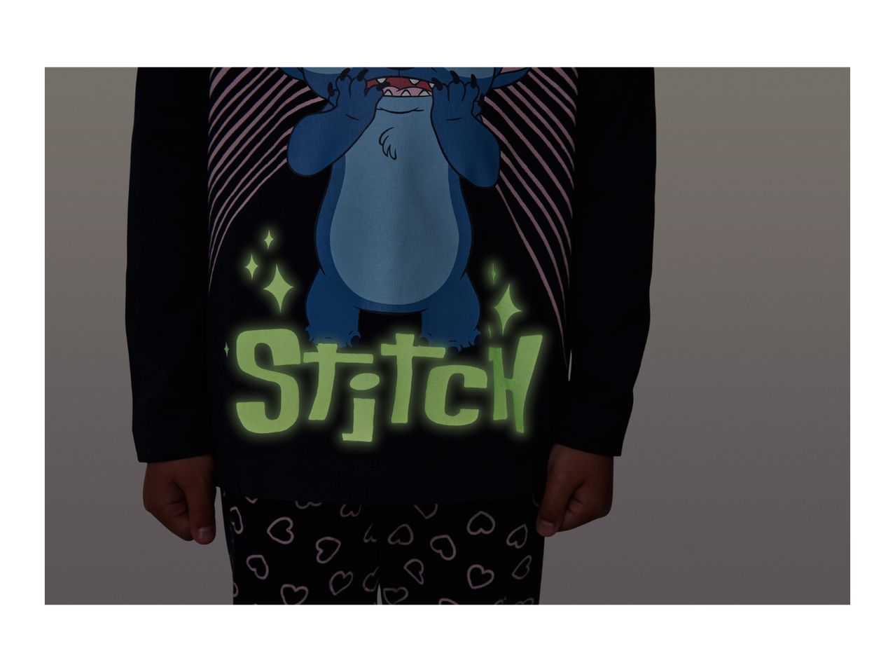 Kids' black Stitch pyjamas with glow-in-the-dark text and heart-patterned bottoms.