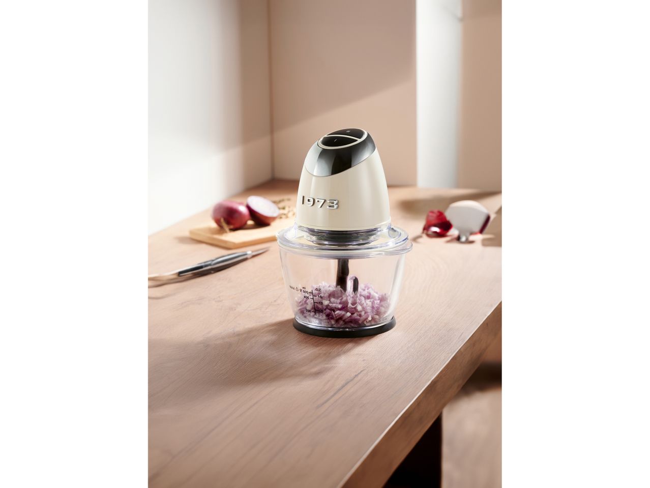 A 1973-branded food chopper with diced red onions on a wooden counter.