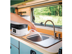 Mini máquina de lavar CLEANMAXX numa autocaravana, mão a despejar água no lava-loiça.