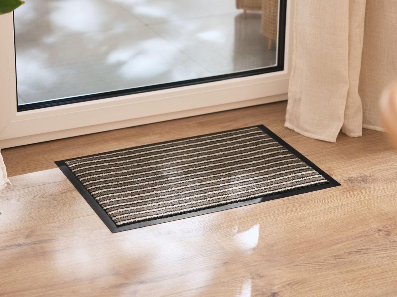 Striped doormat on a wooden floor in front of a glass door.