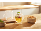 Two glass teacups and a bowl of cookies on a wooden table.