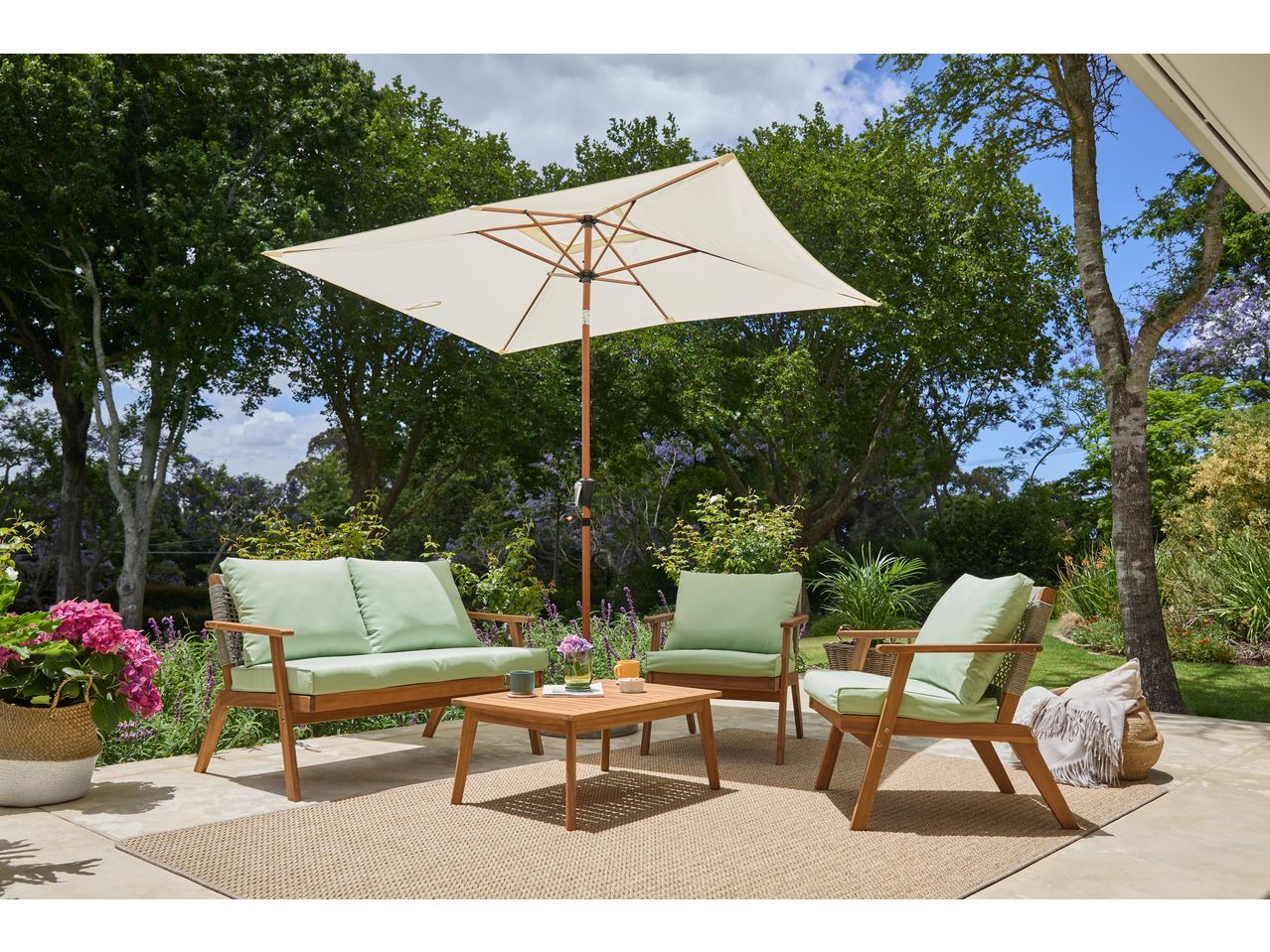 Livarno Crank & Tilt Parasol shading a patio with wooden outdoor furniture and green cushions.