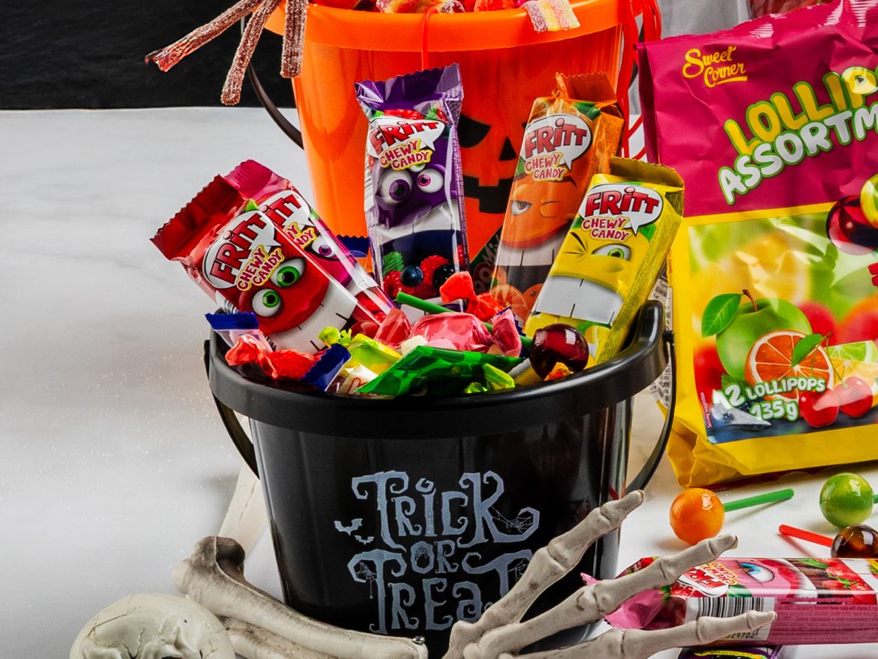 Halloween candy buckets filled with Fritt chewy candies and Sweet Corner lollipops, with skeleton decorations.