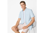 Man in a light blue short-sleeved shirt, white t-shirt, and beige shorts, sitting on a chair.
