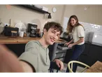 Young couple in a modern kitchen, taking a selfie with an espresso machine.