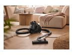 A black vacuum cleaner on a wooden floor in a cozy living room with a sofa and coffee table.