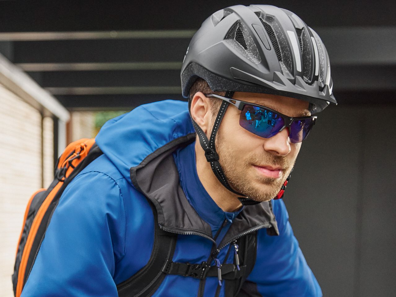 Man in a blue cycling jacket, helmet, and sunglasses with a backpack.