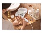 Woman using an electric manicure/pedicure set on her nails, with beauty products nearby.