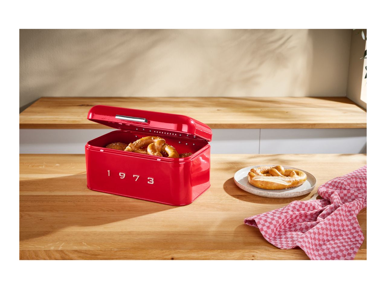 Red retro bread bin with the year 1973 on a wooden countertop next to a pretzel