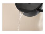 Water pouring from a black cooking pot with a lid against a beige wall.