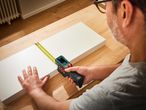 Egy férfi Parkside digitális mérőszalaggal mér egy fehér deszkát.