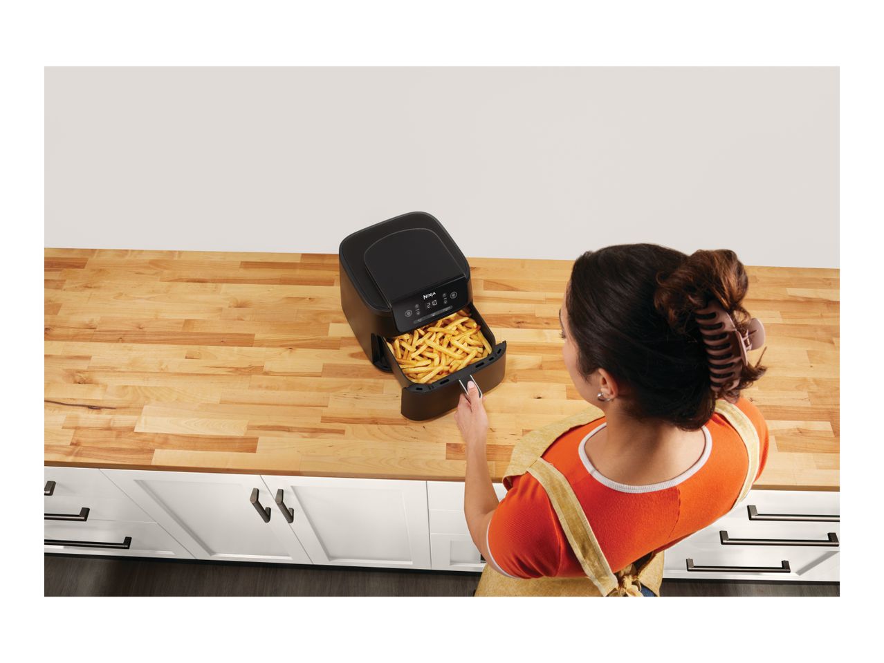 Overhead view of a person pulling out a basket of fries from an air fryer on a kitchen counter.