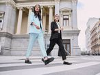 Due donne in abiti eleganti camminano su un attraversamento pedonale davanti a un edificio classico.
