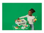 Child playing with a toy barbecue grill and food accessories on a green table.