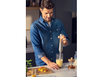 Homem a fazer um batido com uma varinha mágica SILVERCREST 2 em 1, com fruta e mel na mesa.