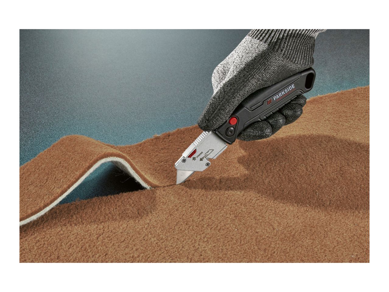 Gloved hand cutting brown carpet with a utility knife.