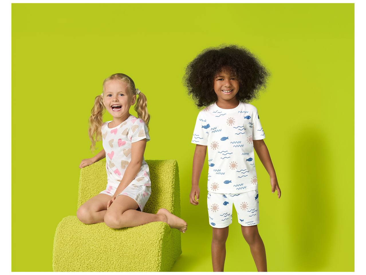 Deux enfants souriants en pyjama d'été, l'un avec des cœurs, l'autre avec des motifs marins.