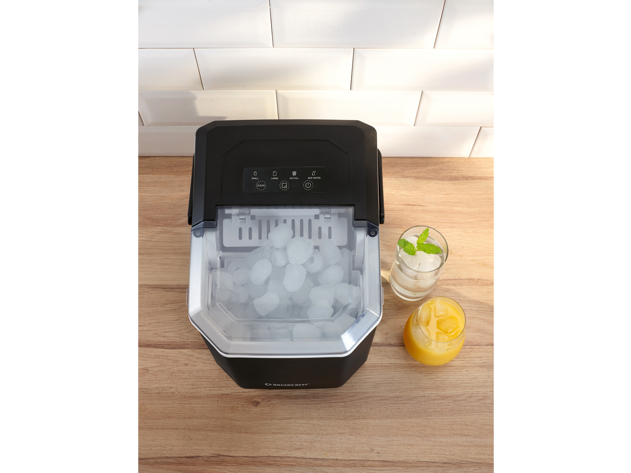 SILVERCREST® Ice Maker with ice, water with mint, and orange juice on a wooden surface.