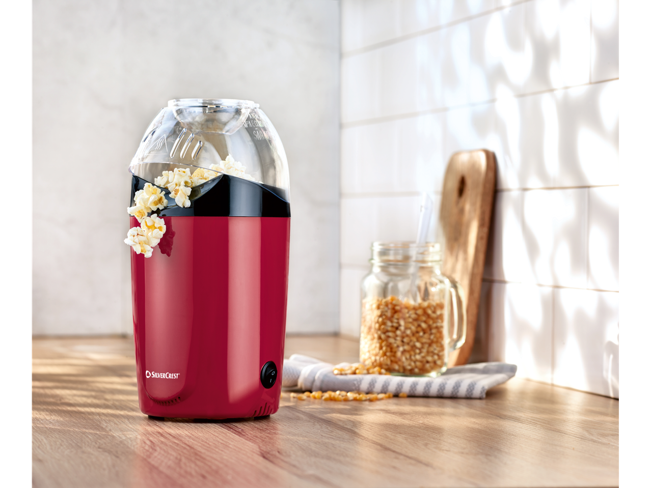 Crveni Silvercrest® aparat za kokice s kokicama na drvenoj ploči.