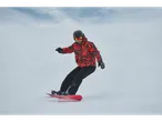 Man snowboarding in a red and black jacket, black pants, helmet, and ski goggles.