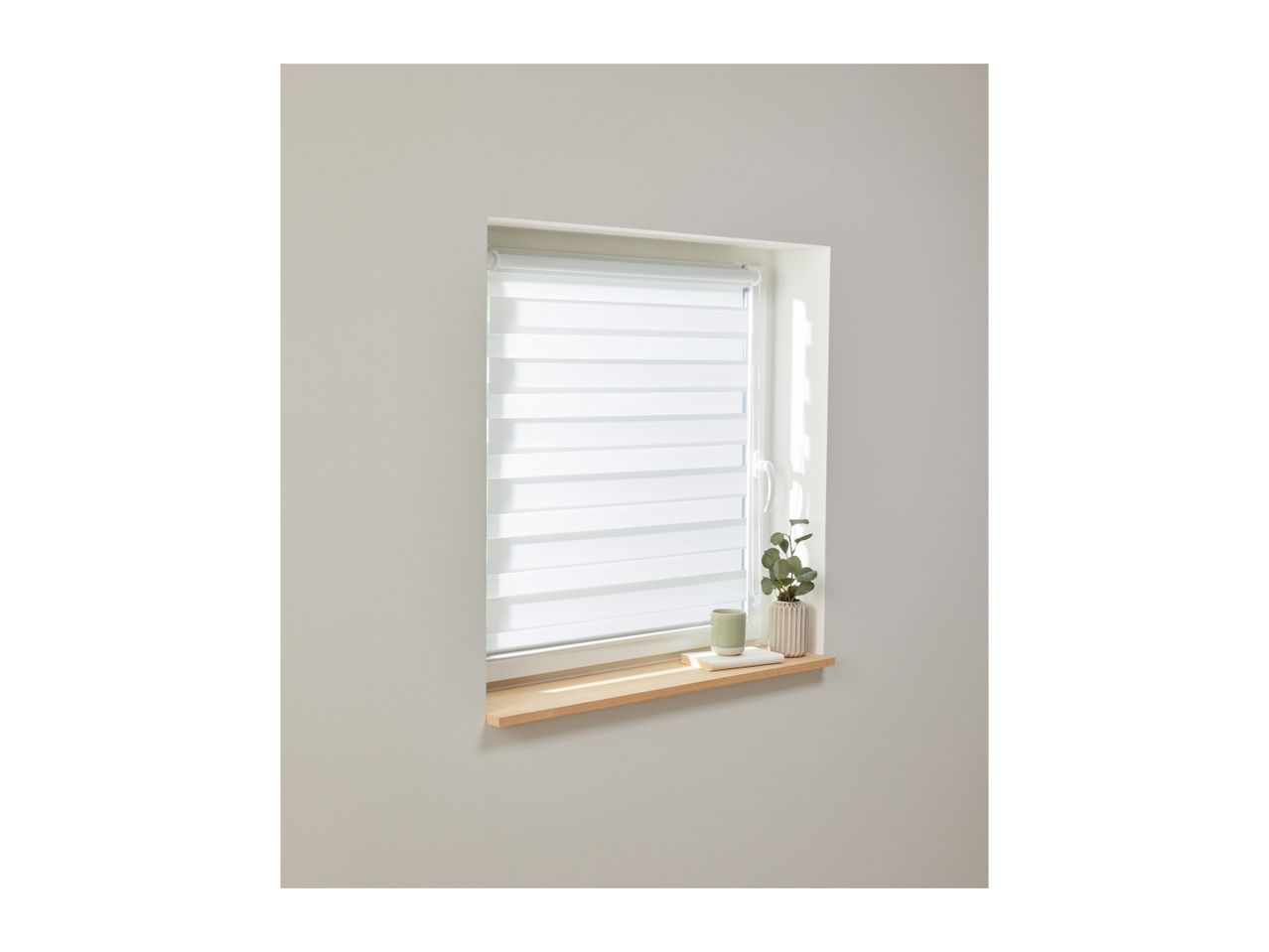 White zebra blinds on a window with a wooden sill, decorated with a plant and mug.