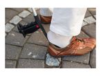 A person using a shoehorn attached to a walking stick to put on a brown shoe.
