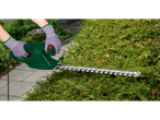 Person trimming a hedge with a green electric hedge trimmer.