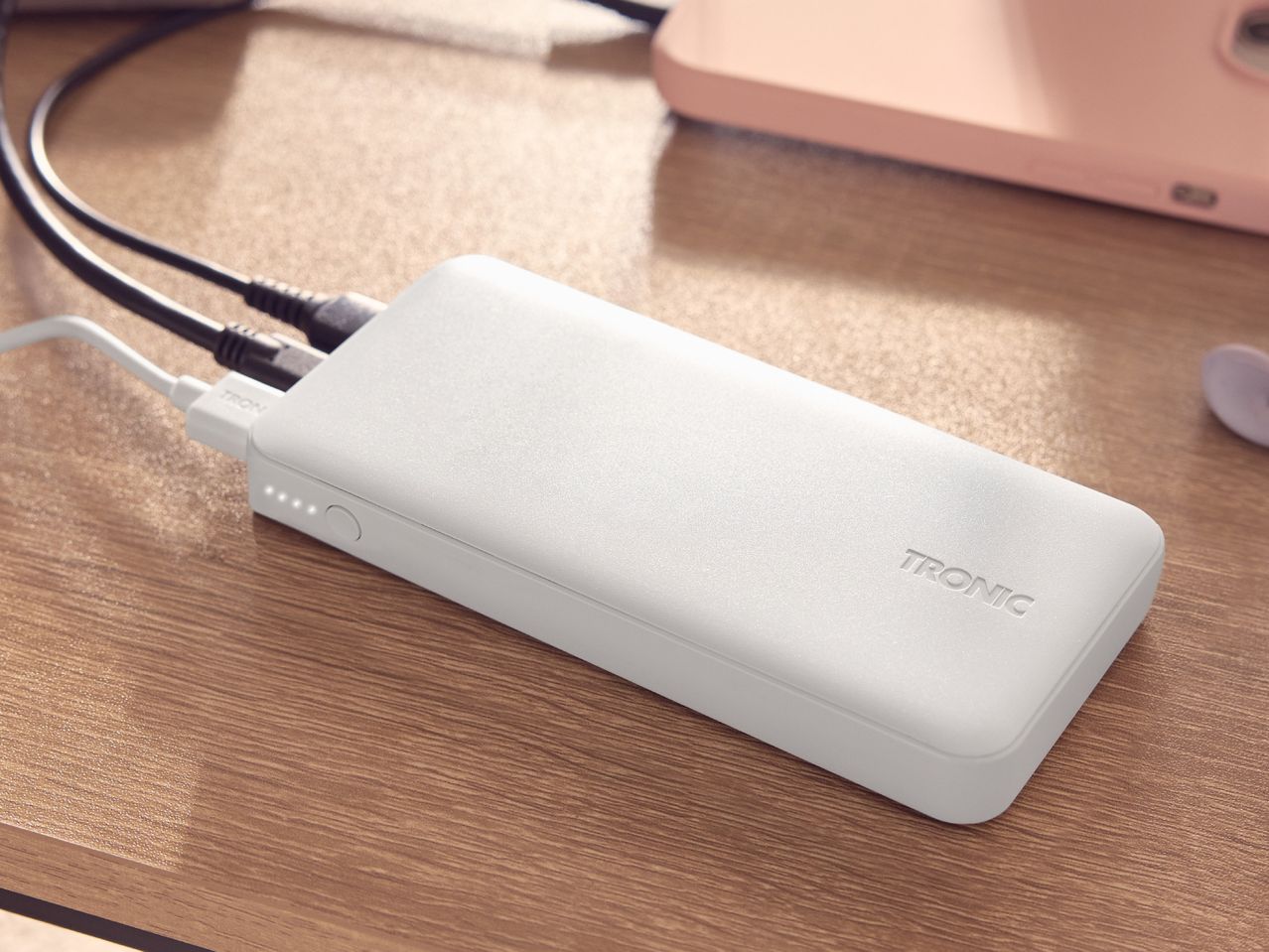 White power bank charging on a wooden surface, with a pink phone in the background.