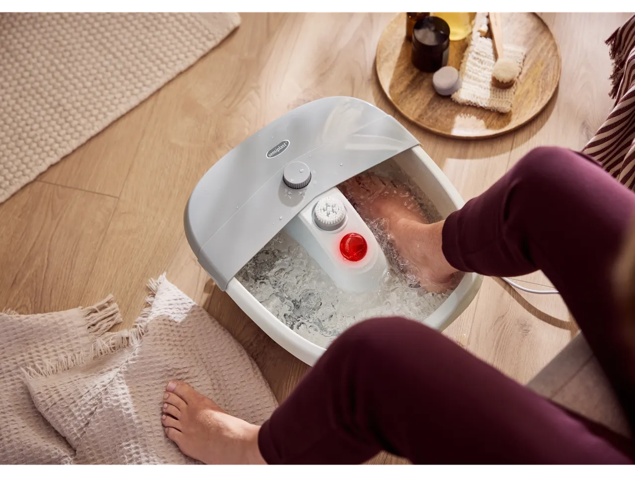 A person soaking their feet in a SENSIPLAST® foot bath with water on a wooden floor.